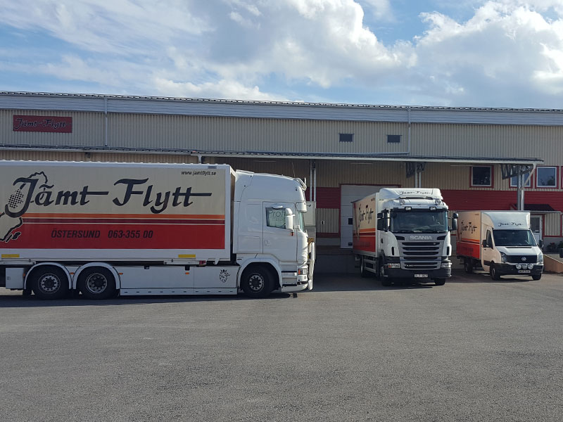 jamtflytt-lokaler Tre Jämt Flytt-lastbilar parkerade utanför företagets lagerbyggnad, med logotyp och kontaktuppgifter tydligt synliga på sidorna.