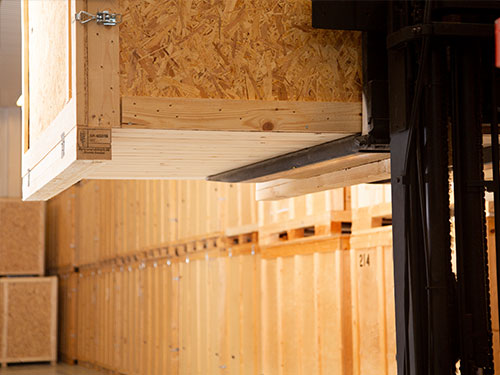 start-magasinering-2 Gaffeltruck lyfter en träbox i ett stort magasin med rader av staplade förvaringsboxar.