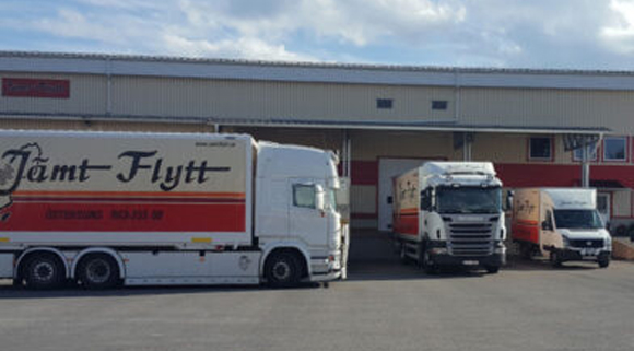 lastbilar Tre Jämt Flytt-lastbilar parkerade utanför företagets lagerbyggnad, med logotyp och kontaktuppgifter tydligt synliga på sidorna.
